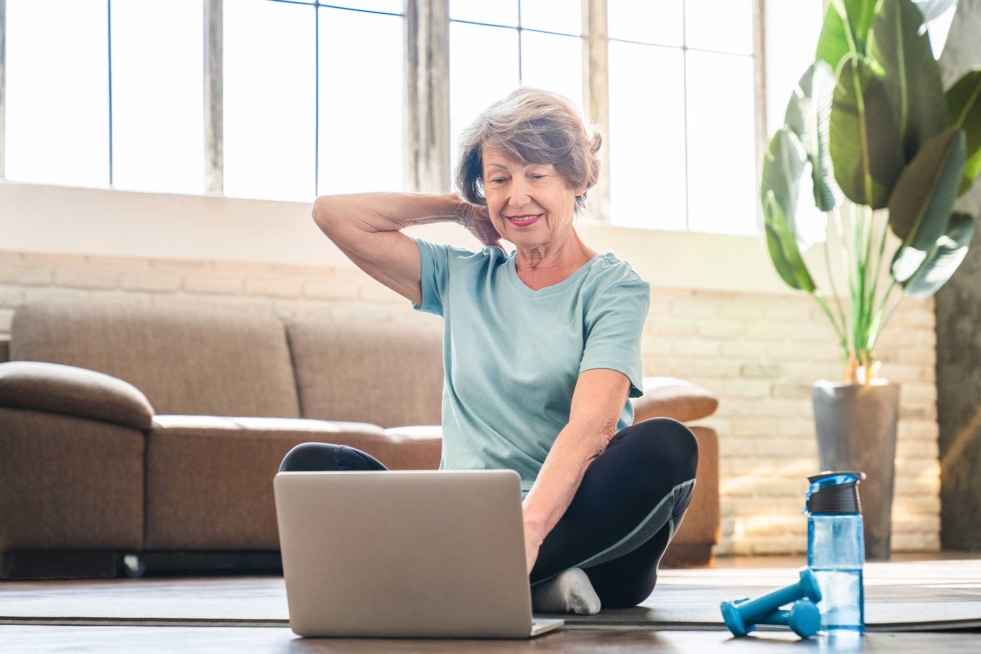 ergoflix-semaine-bleue-ellii-ateliers Grand-mère sportive faisant du sport sur un tapis de fitness en tenue d'entraînement tout en utilisant un ordinateur portable pour un tutoriel vidéo en ligne. Personnes âgées actives, amincissement du corps