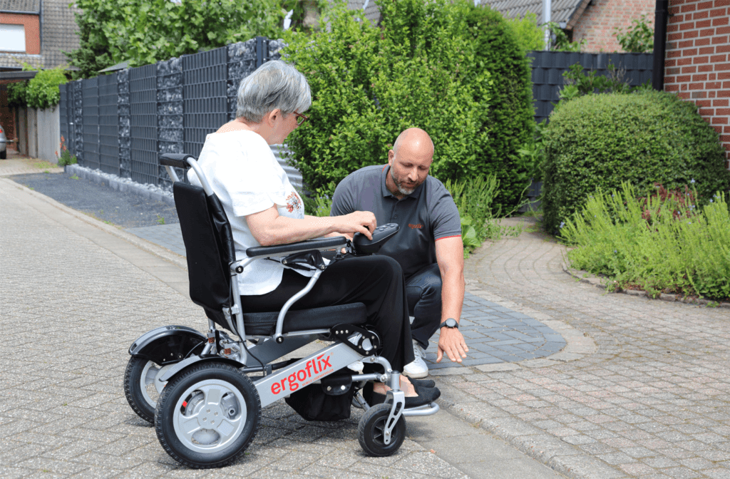 Un conseiller présente un fauteuil roulant électrique ergoflix à une cliente devant chez elle