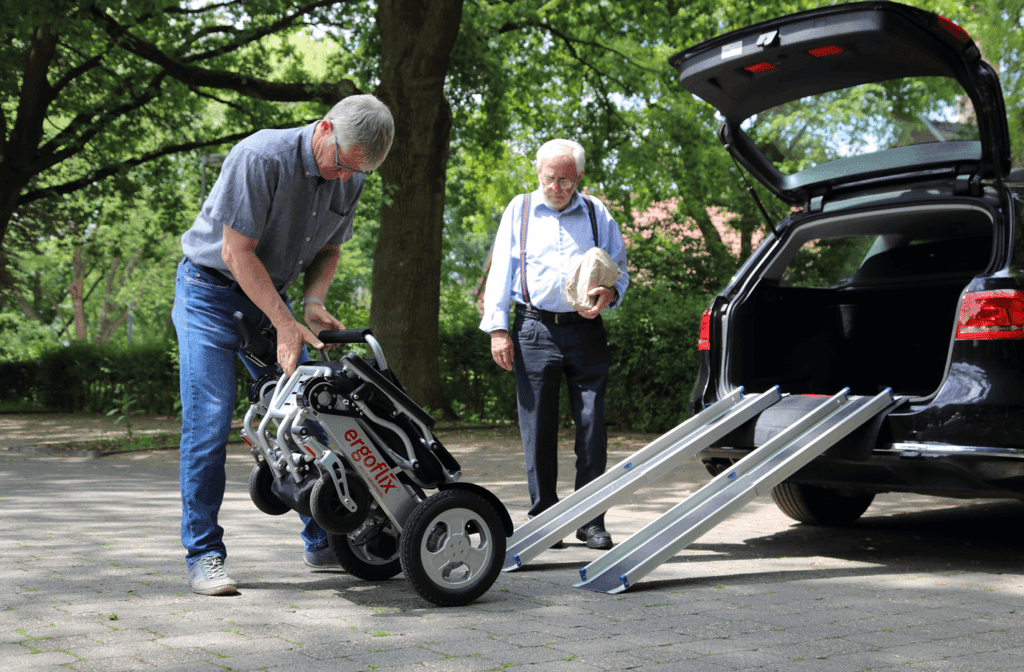Un homme charge un fauteuil roulant électrique ergoflix plié dans un coffre à l’aide d’une rampe