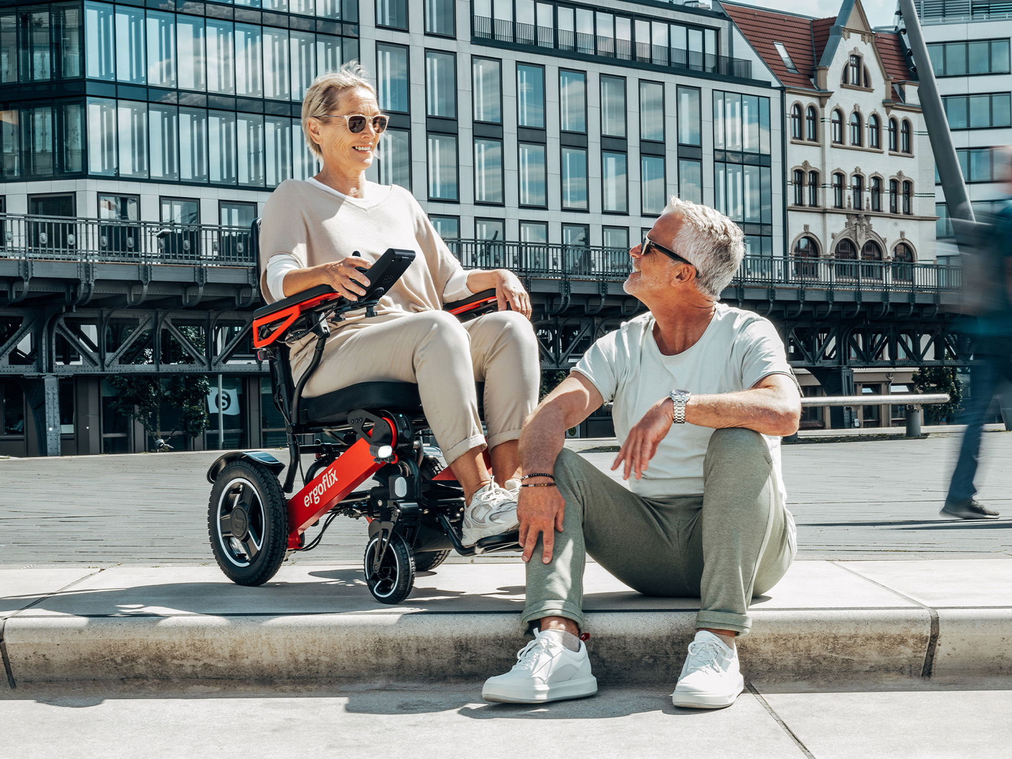 Femme en fauteuil roulant électrique ergoflix discutant avec un homme sur une promenade au bord de l’eau